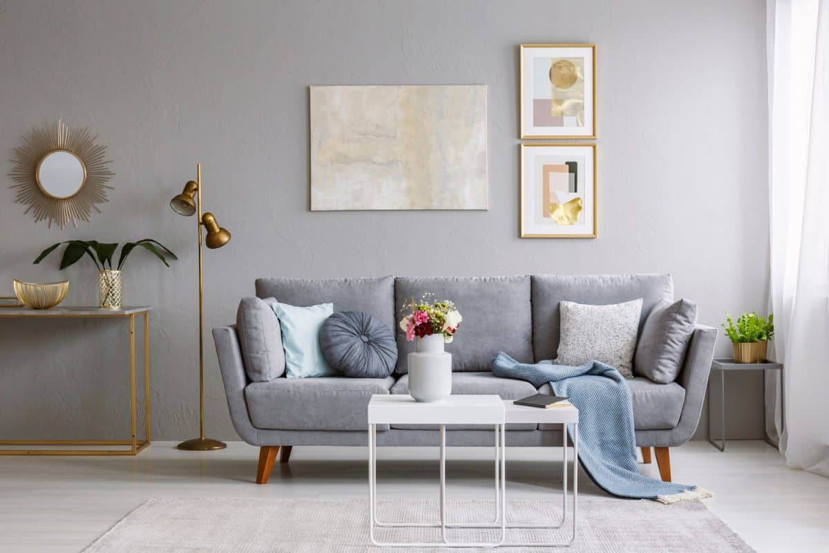 Grey sofa with pillows and blanket standing in bright living room interior with gold lamp, fresh flowers on white table and carpet on the floor, What Is Most The Popular Color For The Living Room?