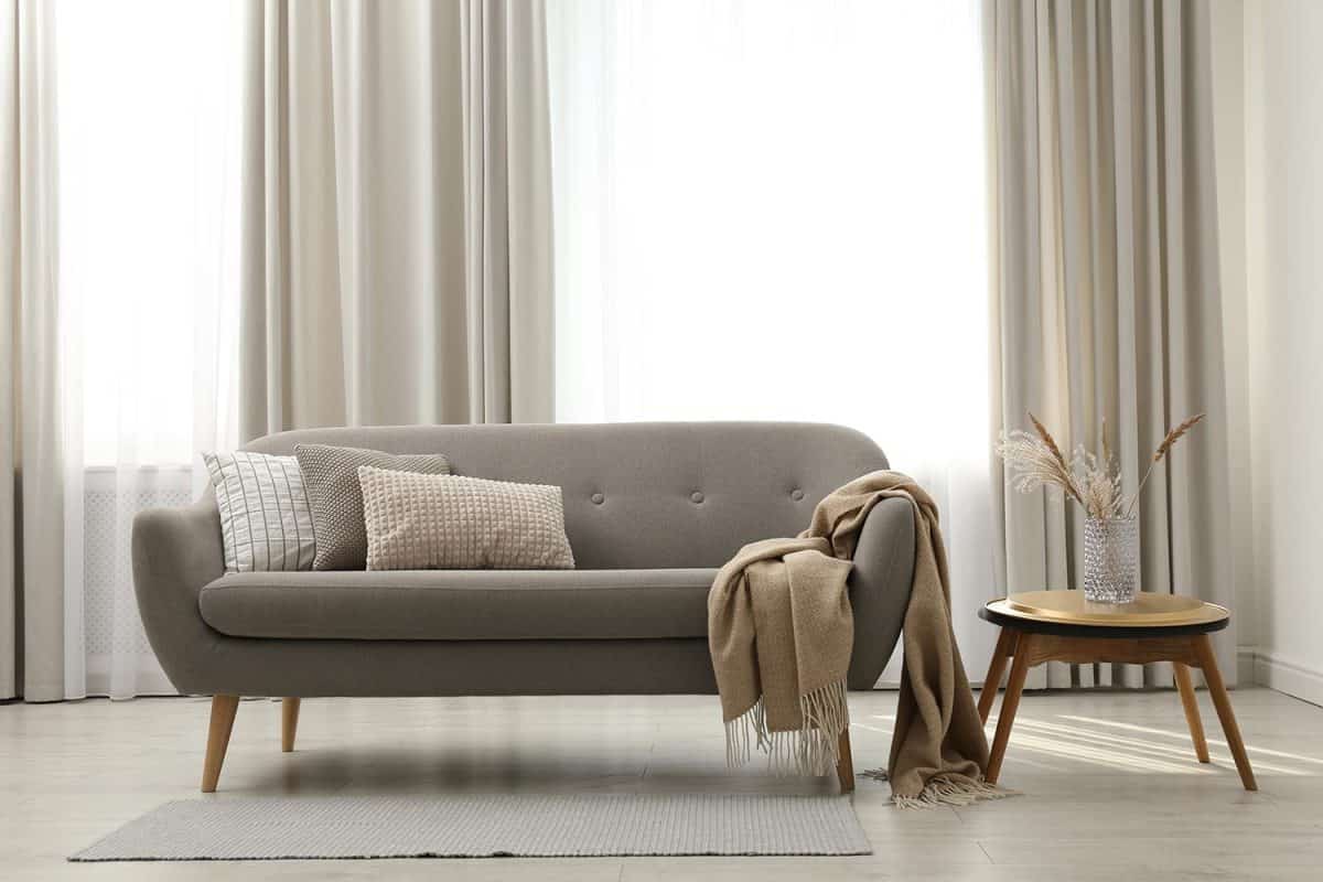 Grey sofa with pillows near window in stylish living room interior