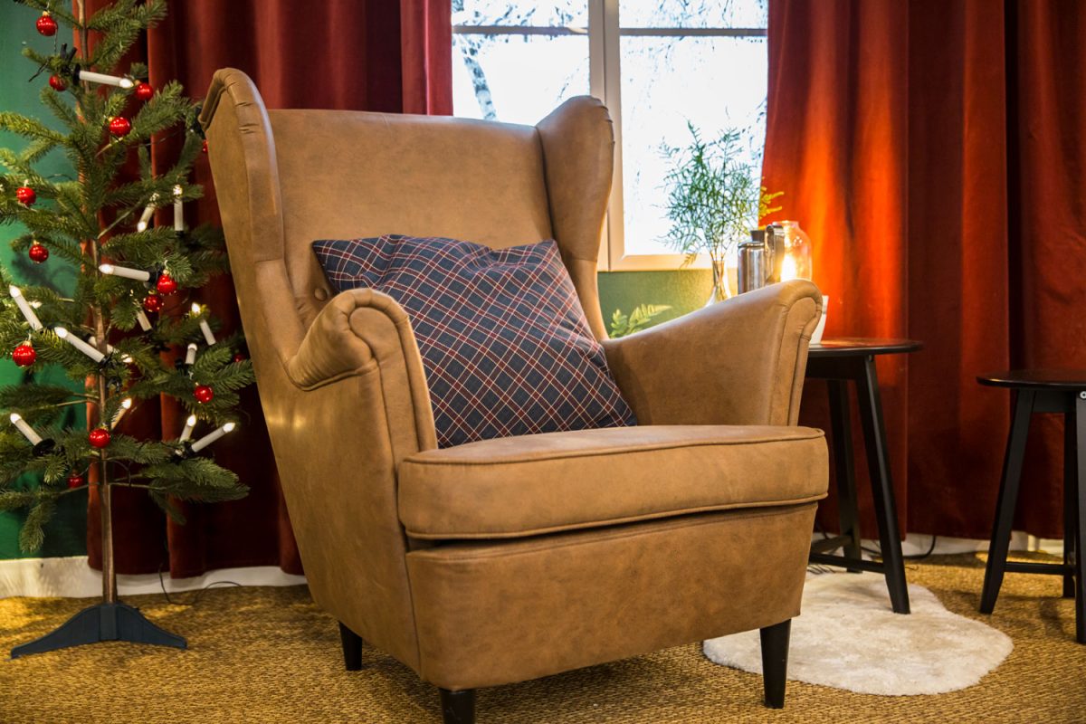 A big leather accent chair with a patterned throw pillow and a Christmas tree on the side
