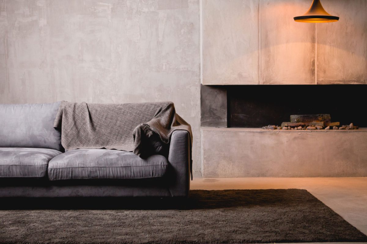 A black sectional sofa with a brown throw pillow and a fireplace on the side