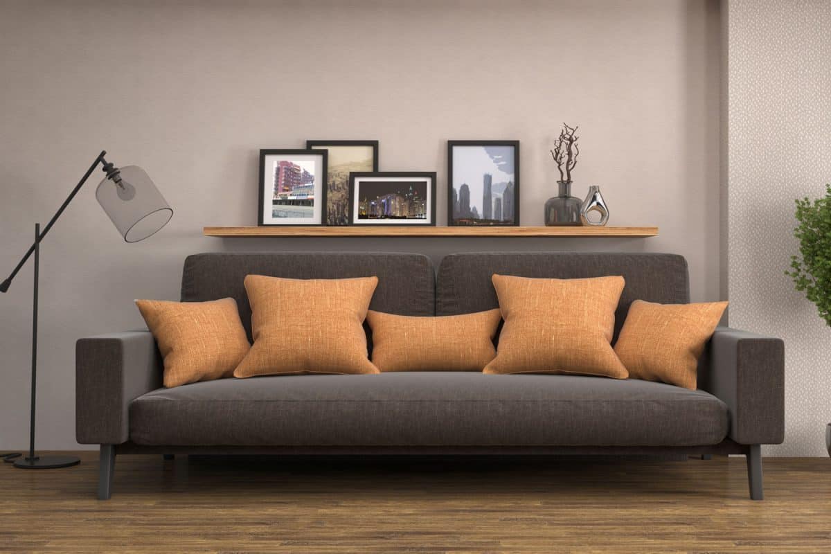 A black sofa matched with orange throw pillows and dark tan wall with picture frames