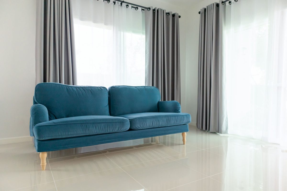 A blue couch inside a white living room with gray curtains