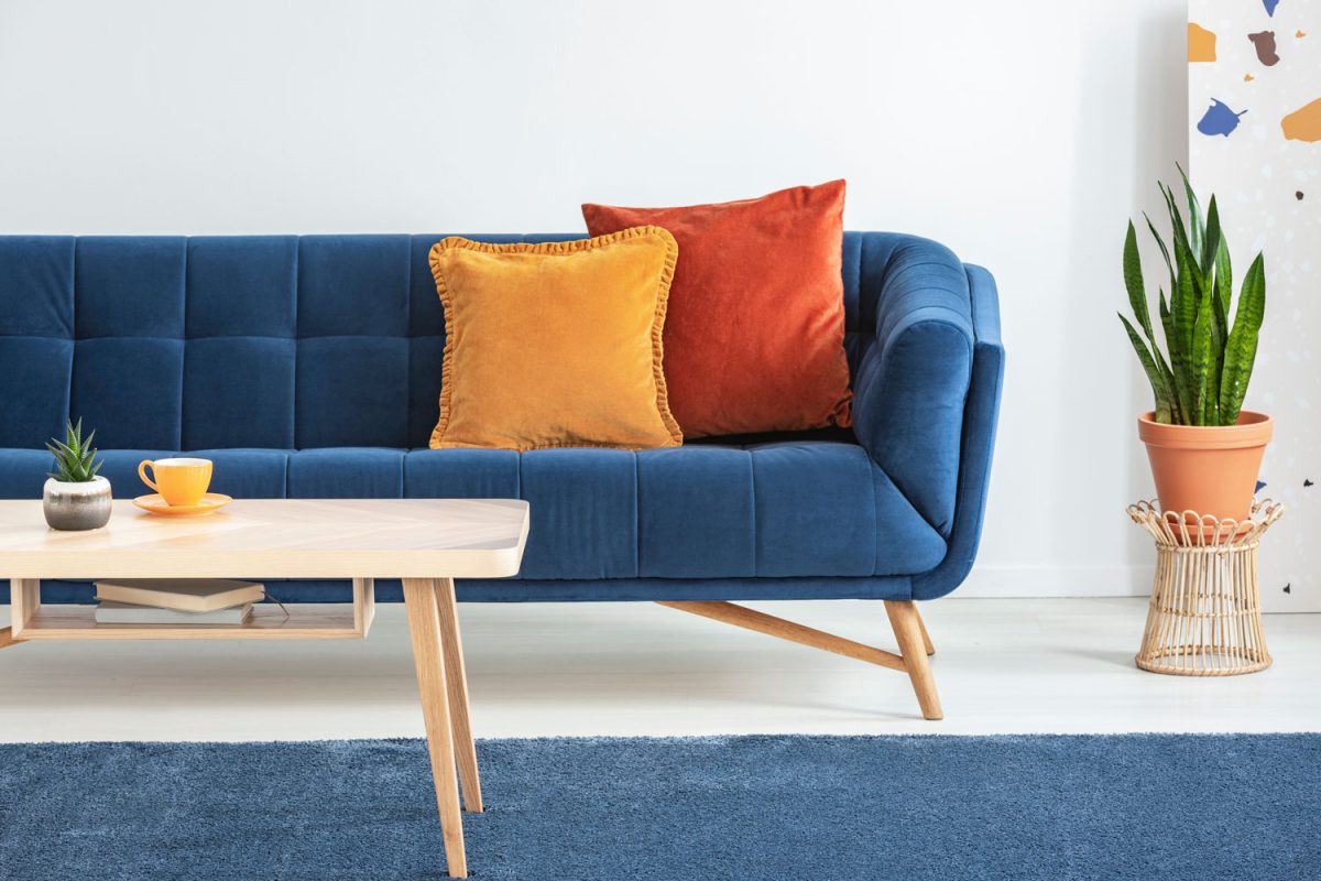A blue couch with orange and red colored throw pillows matched with wooden furnitures