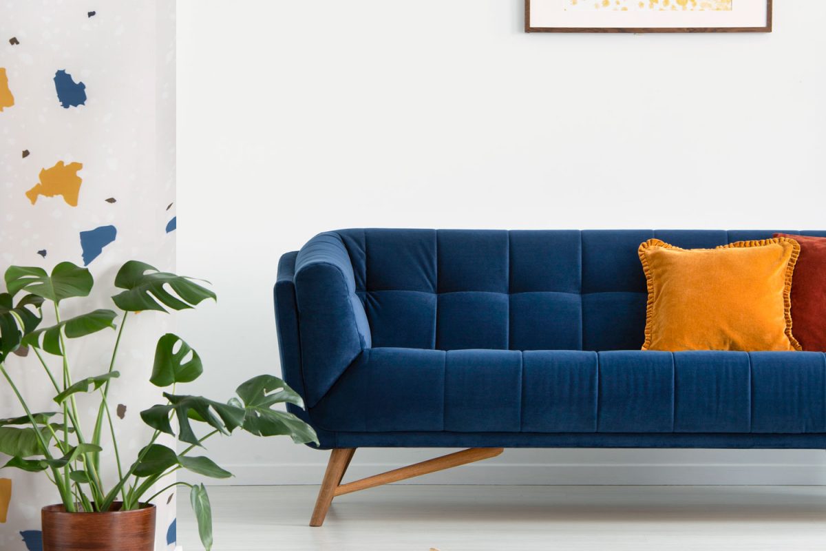 A blue sectional couch with a yellow throw pillows inside a white living room