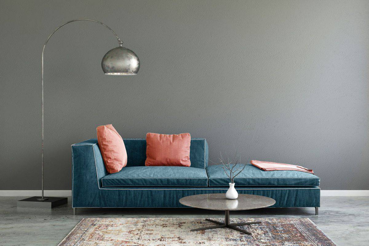 A blue sofa with light pink throw pillows with a dangling lamp on the side in a gray living room