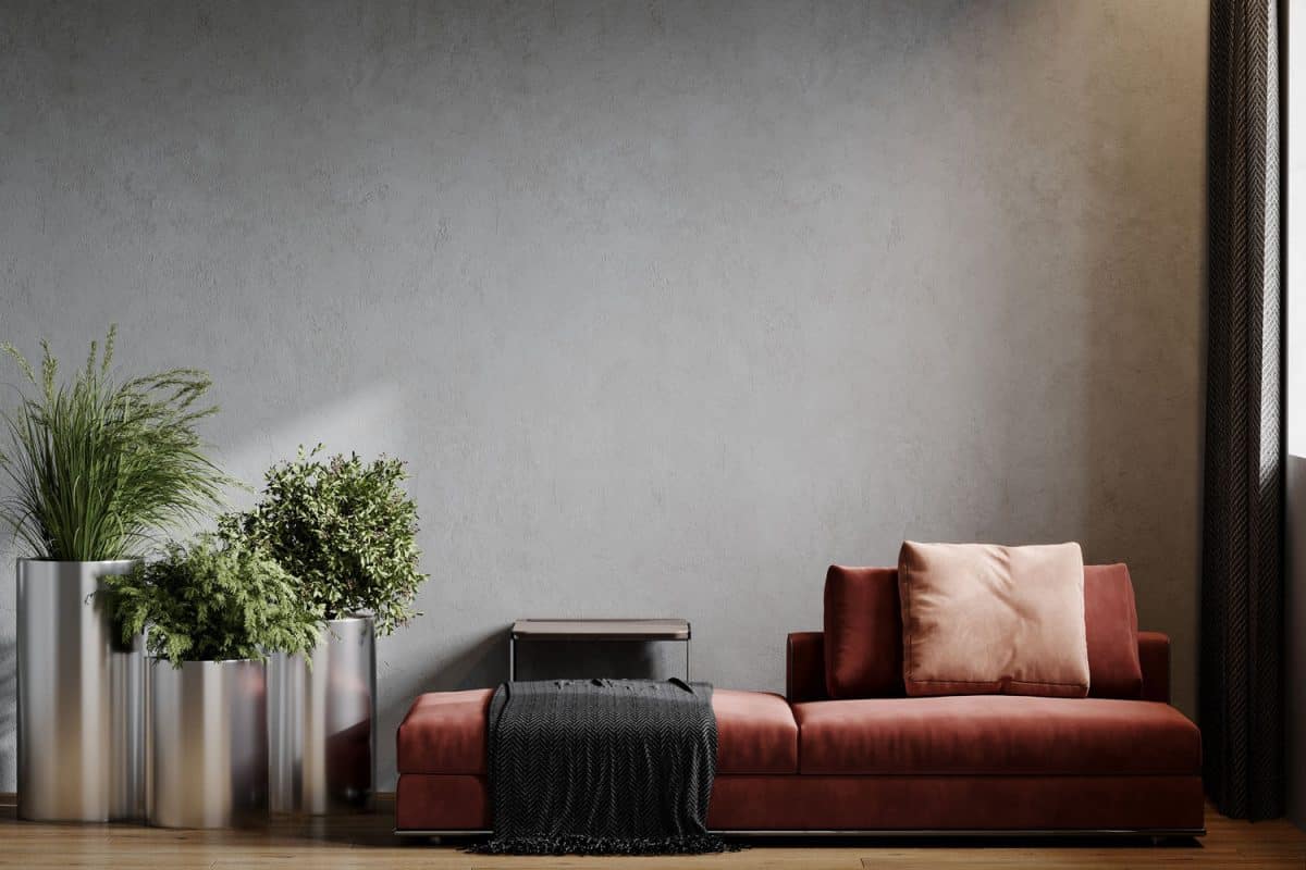 A burgundy colored sofa with matching throw pillows and plants on the side held against a gray wall