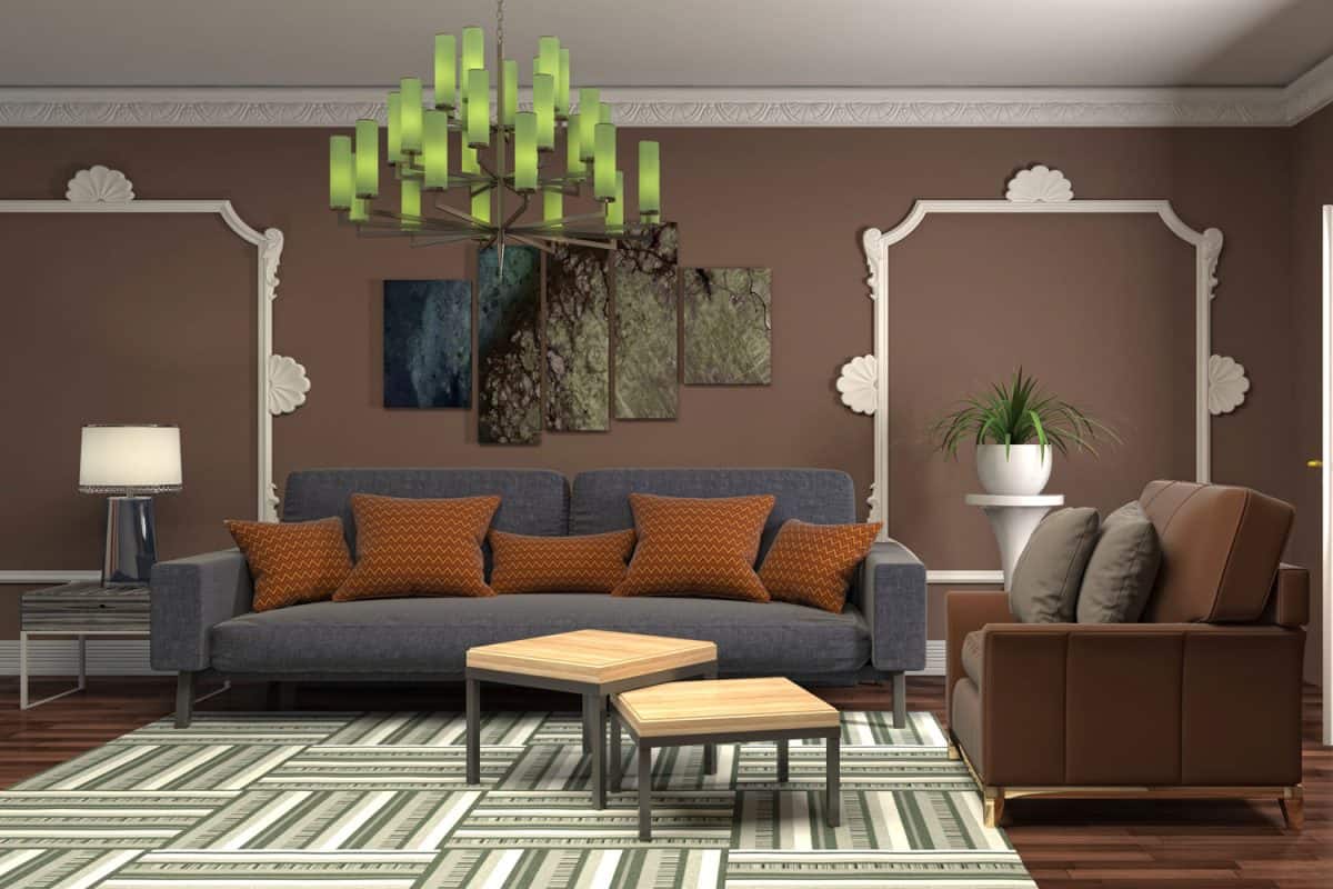 A dark blue sofa with orange throw pillows and brown armchair with green patterned carpet