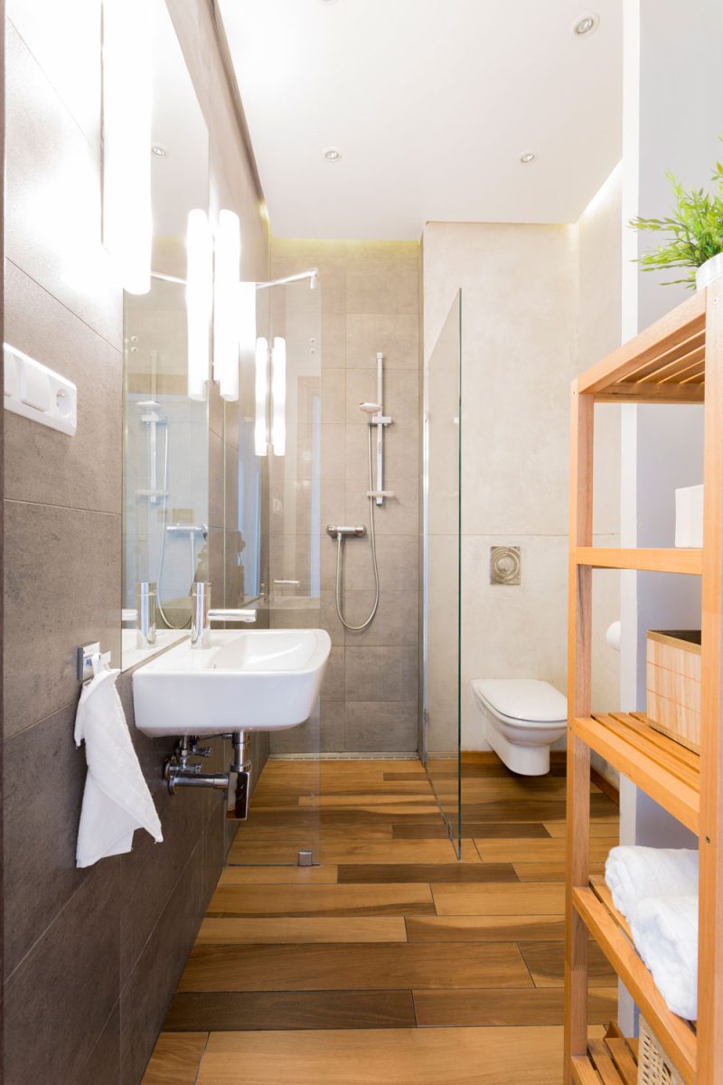 A gorgeous rustic bathroom with wooden cabinet area for towels and a glass wall shower area