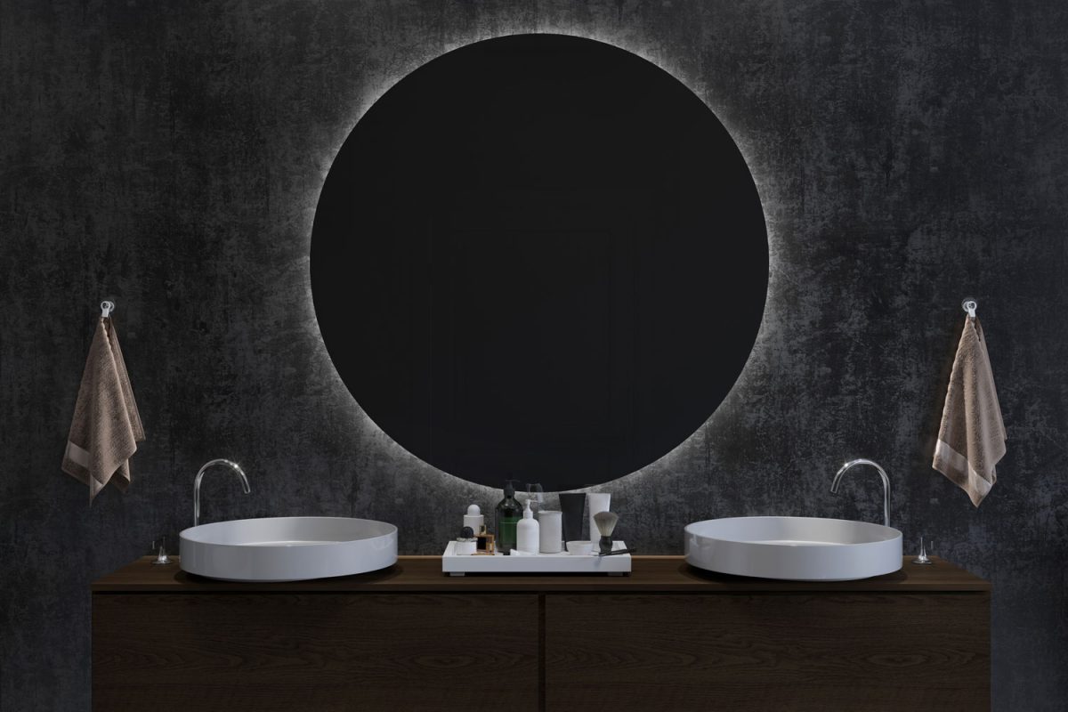 A huge backlighted mirror inside a dark designed bathroom with a wooden paneled vanity cabinet