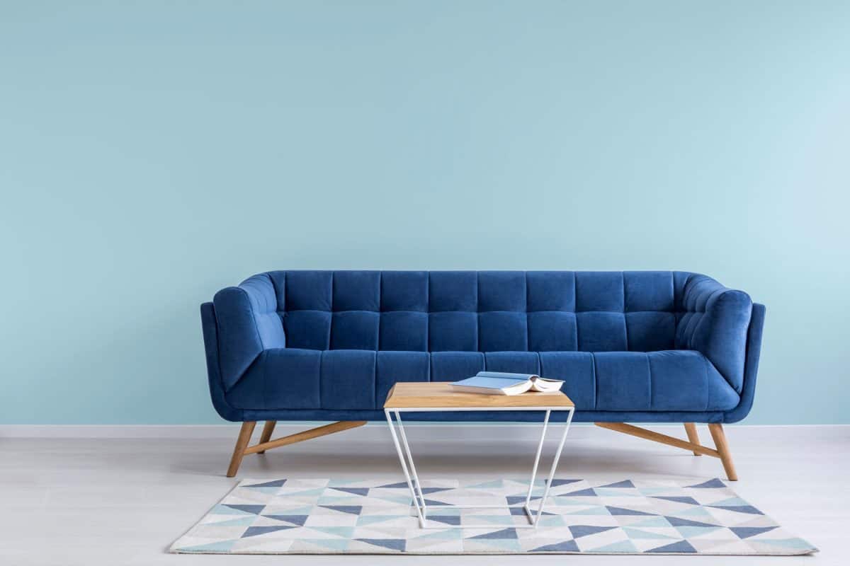 A long blue sleeper sofa with wooden pegs and a patterned blue carpet