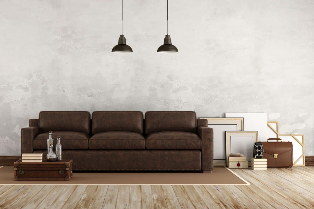 A long brown sofa and empty paint canvases on the side in a living room with wooden flooring