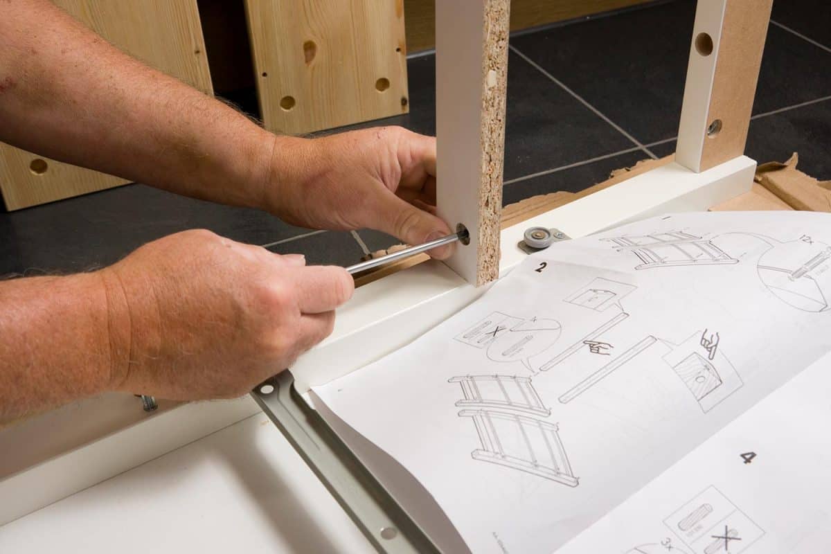 A man follows instructions to build an IKEA flat-pack chest of drawers at home