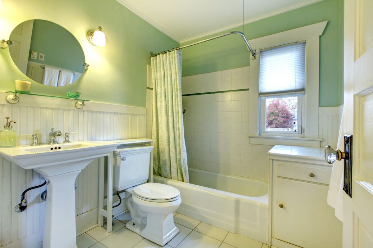 A mint green bathroom with white tile walls matched with a green shower curtain