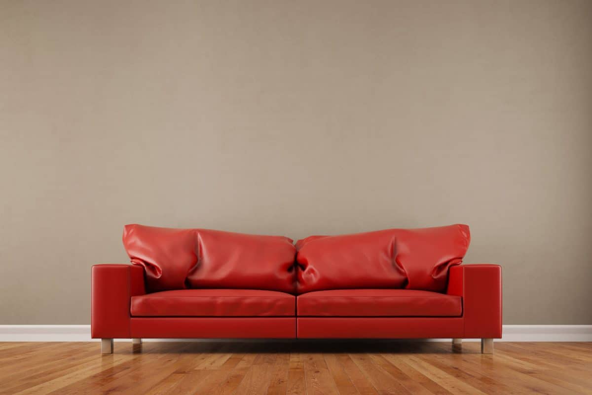 A red leather sofa with laminated flooring in a brown colored living room