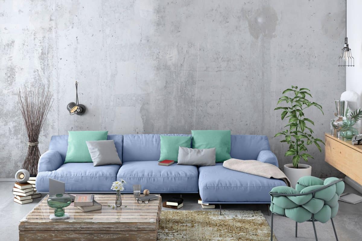 A sectional sofa with light blue colored throw pillows inside a cement living room