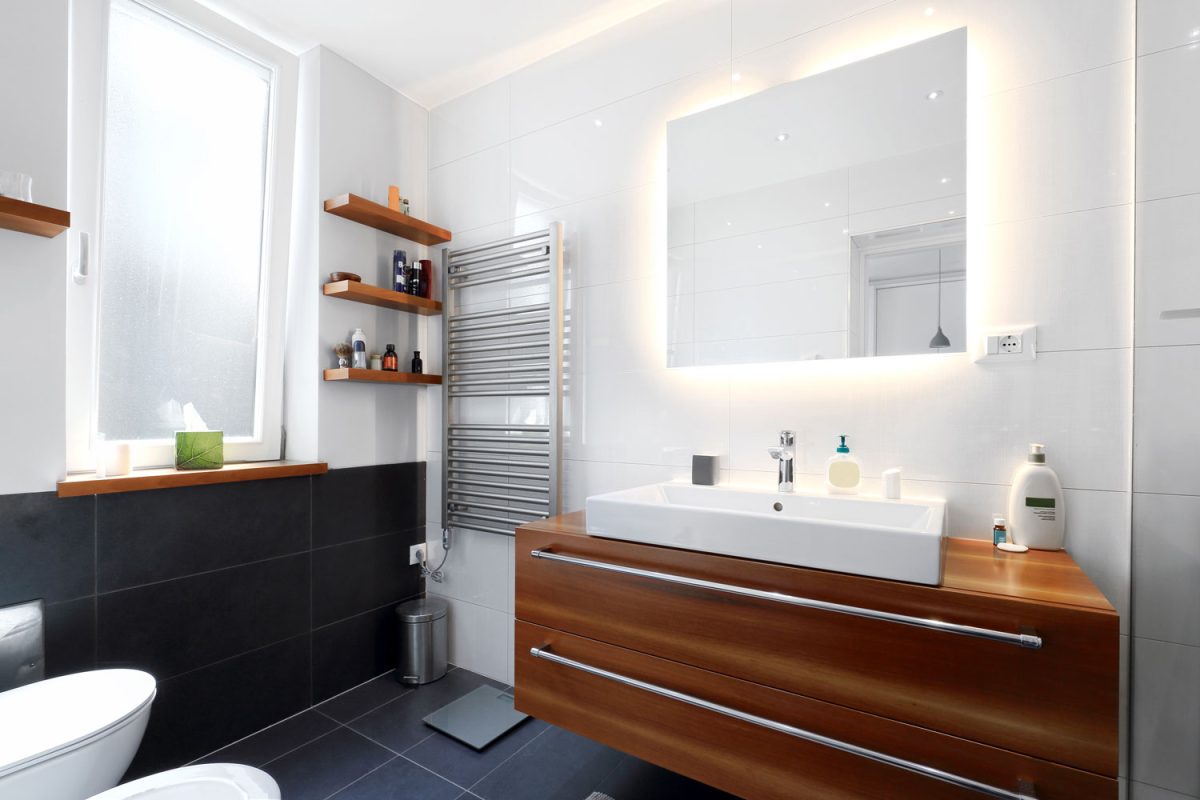 A small modern bathroom with a wooden cabinet vanity and a mirror with backlight