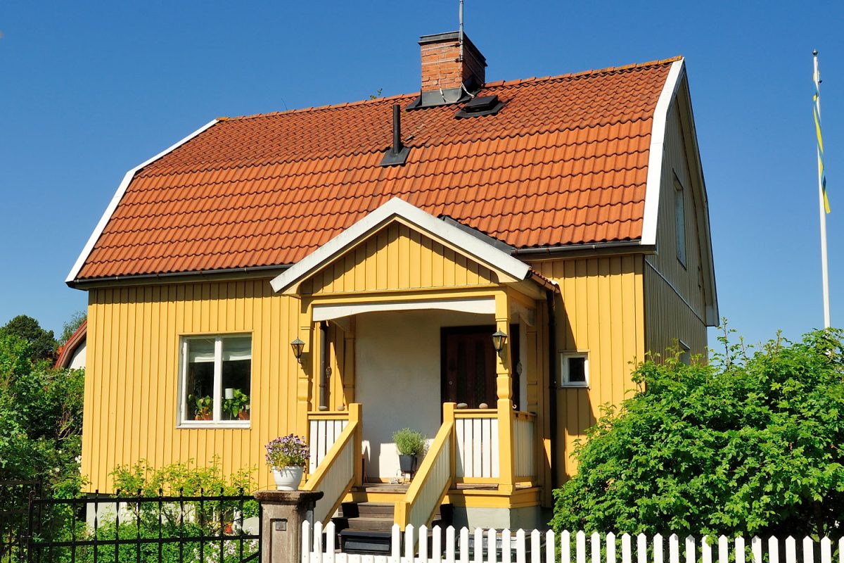 A small yellow wooden siding barn house with clay tile roofing