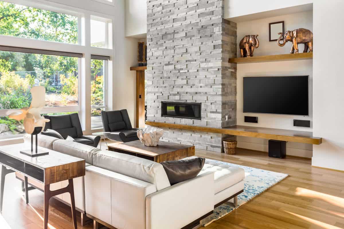 A tall stone cladding on the fireplace with wooden flooring and white leather sofa