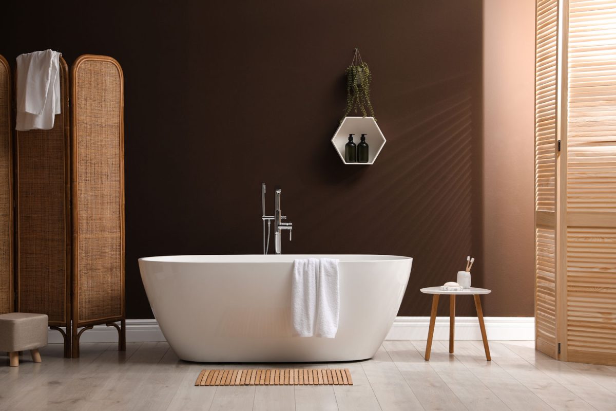 A white bathtub inside a brown and rustic inspired bathroom with laminated flooring