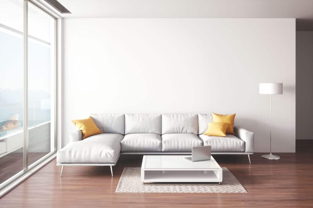 A white sectional sofa with yellow throw pillows inside a wooden laminate living room
