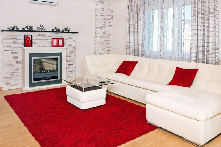 A white sofa matched with red throw pillows and a red carpet next to the fireplace, What Color Couch Goes With Red Carpet?