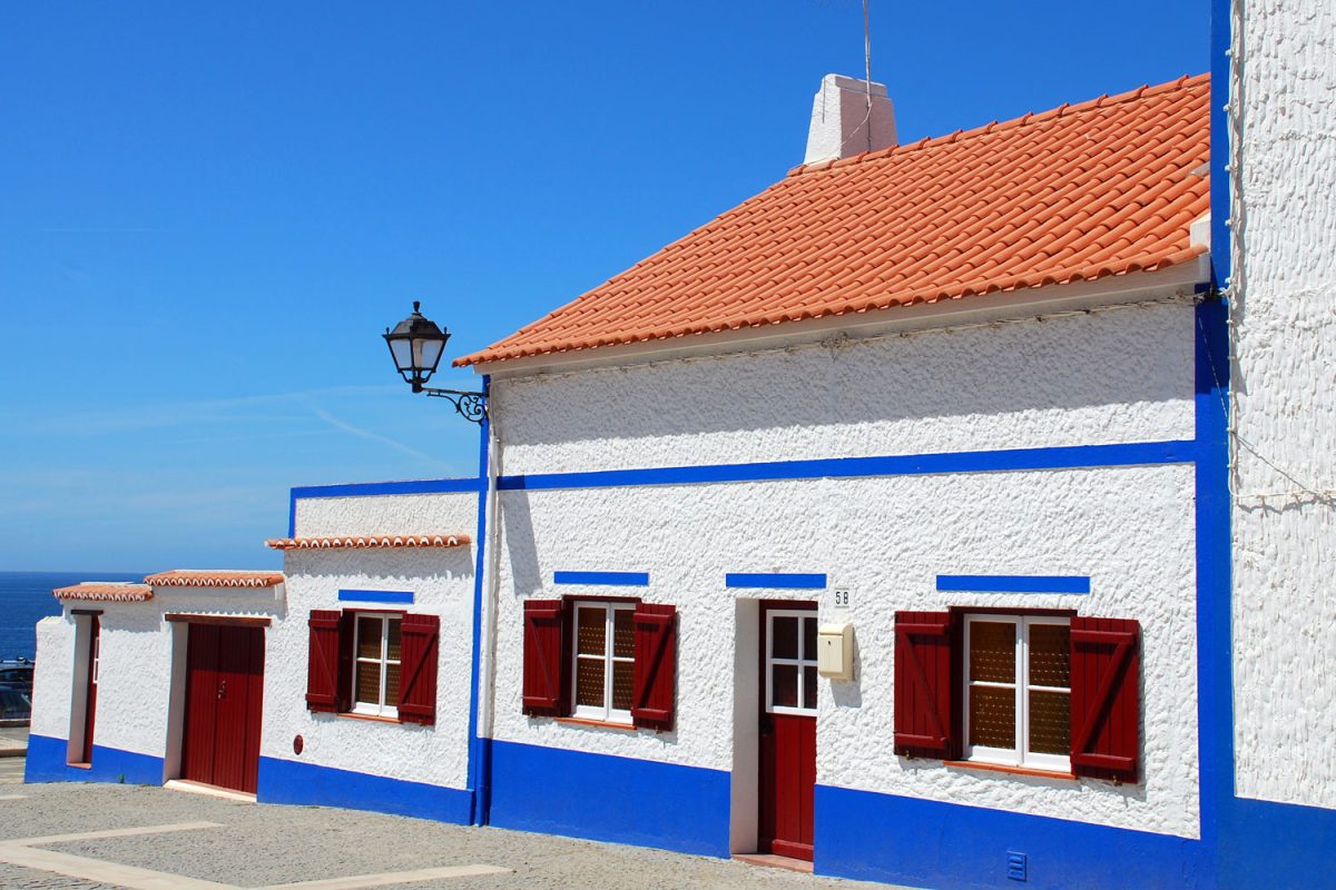A white stucco wall house with red window shutters and blue painted trims matching the red clay tile roofing