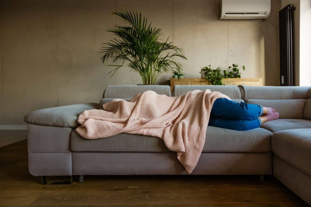 A woman covering herself with a pink blanket while sleeping on the sofa