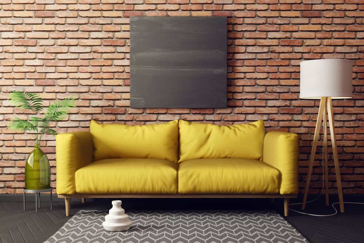 A yellow sleeper sofa placed against a brown brick wall