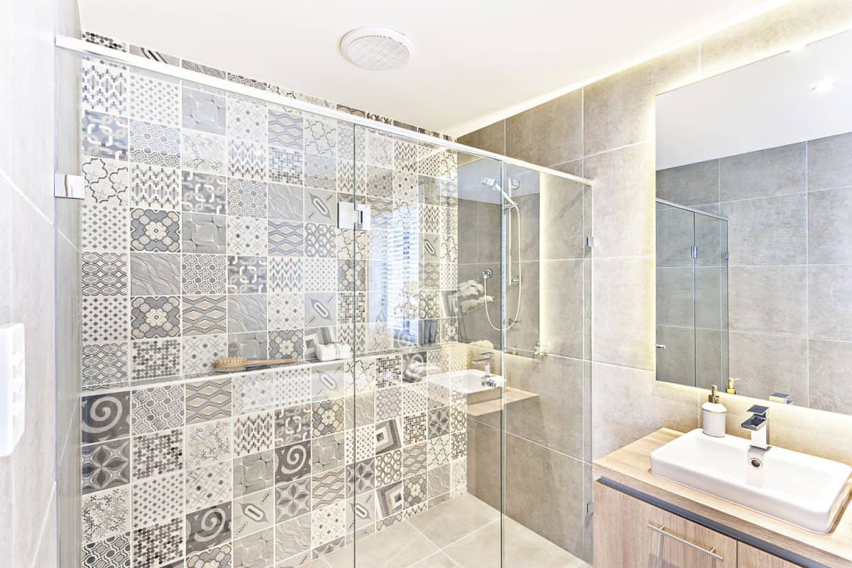 Bathroom pattern wall design with art printed on the wall in the shower area which covered with glass panels under the white ceiling and walls