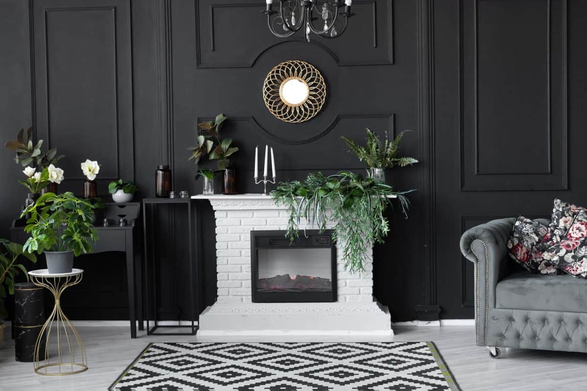 Black and white inspired living room with black flat panel walls, white brick mantel fireplace and plants scattered on the living room