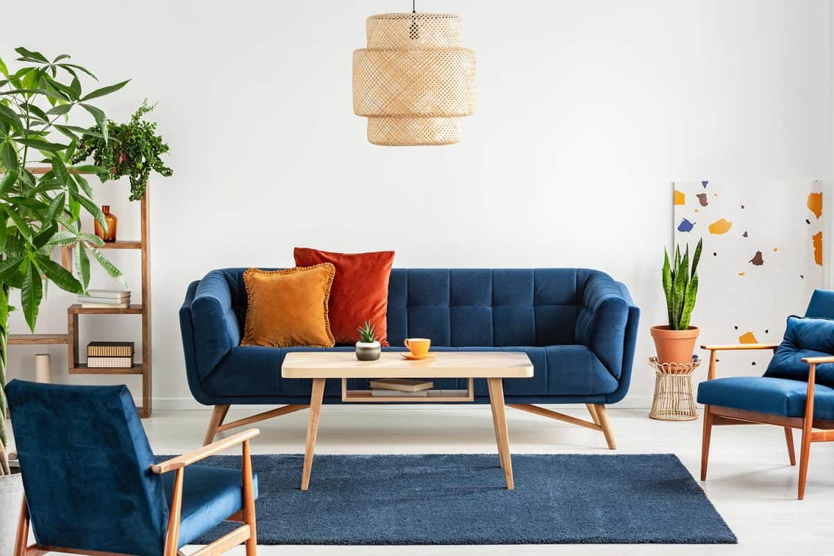Blue wooden armchairs and couch in living room interior with plants and lamp above table