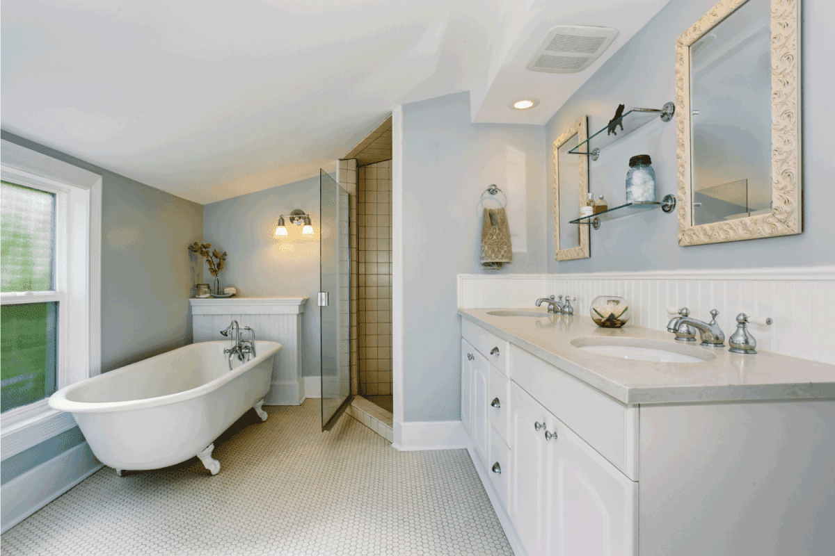 Elegant bathroom in pastel blue tones with white bath tub, cabinets and shower.