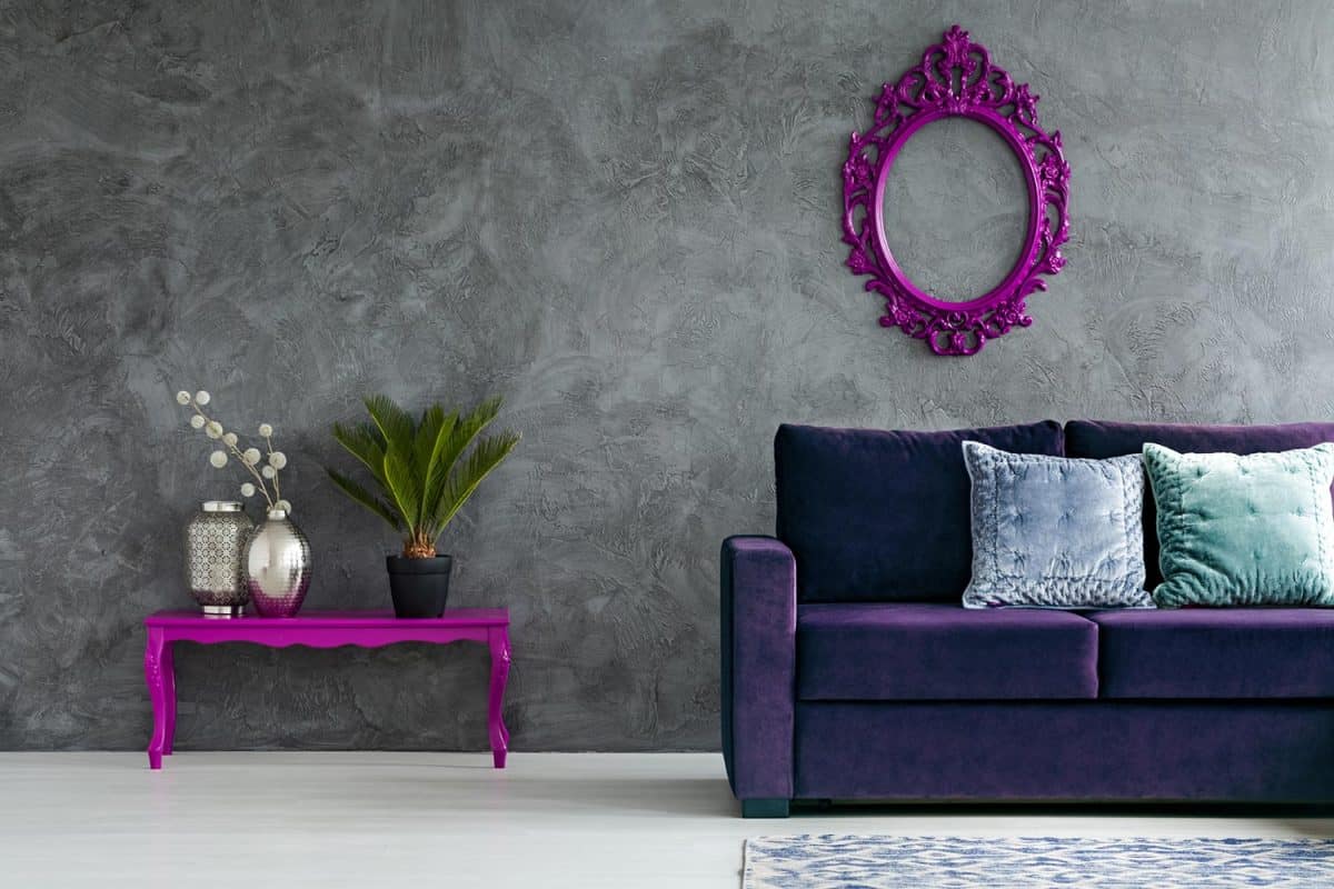 Front view of living room interior with velvet sofa, table with plant and silver vases, vintage frame and concrete wall
