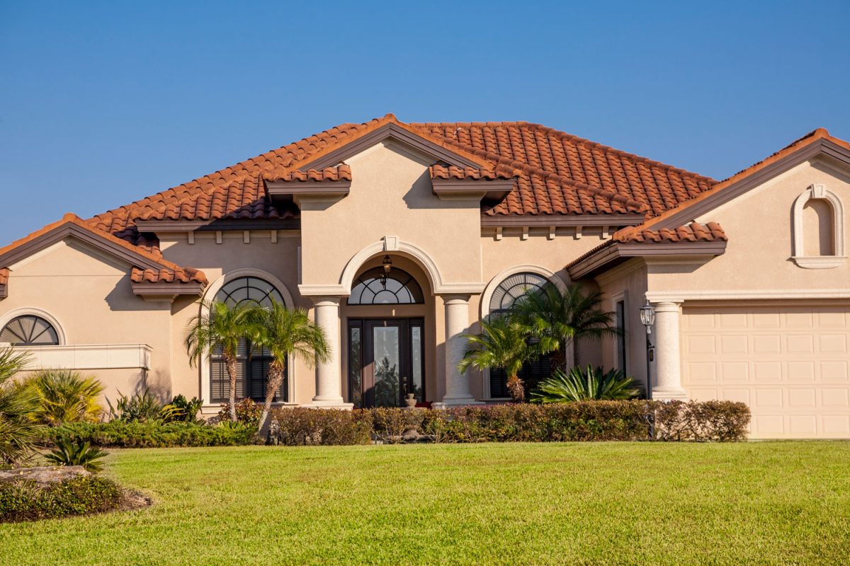 Huge mansion with clay tile roofing, stucco exterior walls and gorgeous landscaping on the lawn