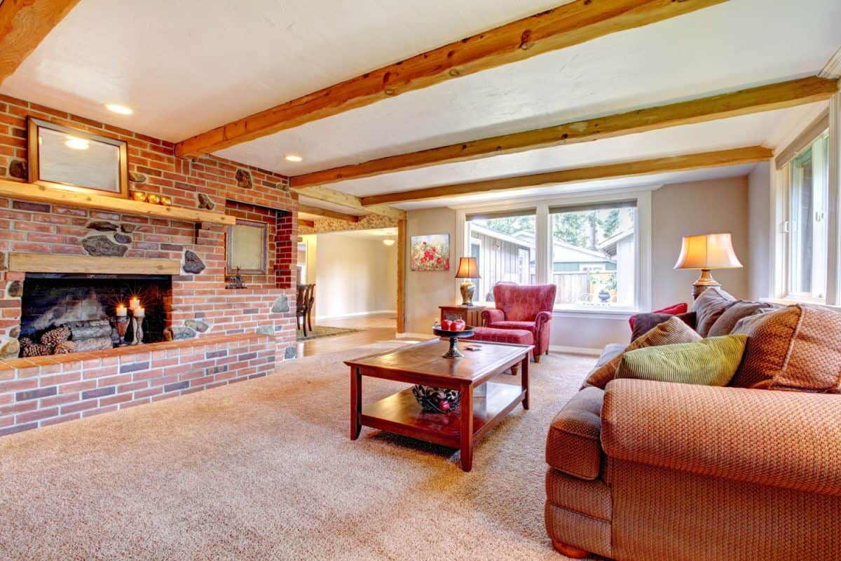 Interior of a carpeted flooring house with a brick fireplace with wooden trusses and white ceiling