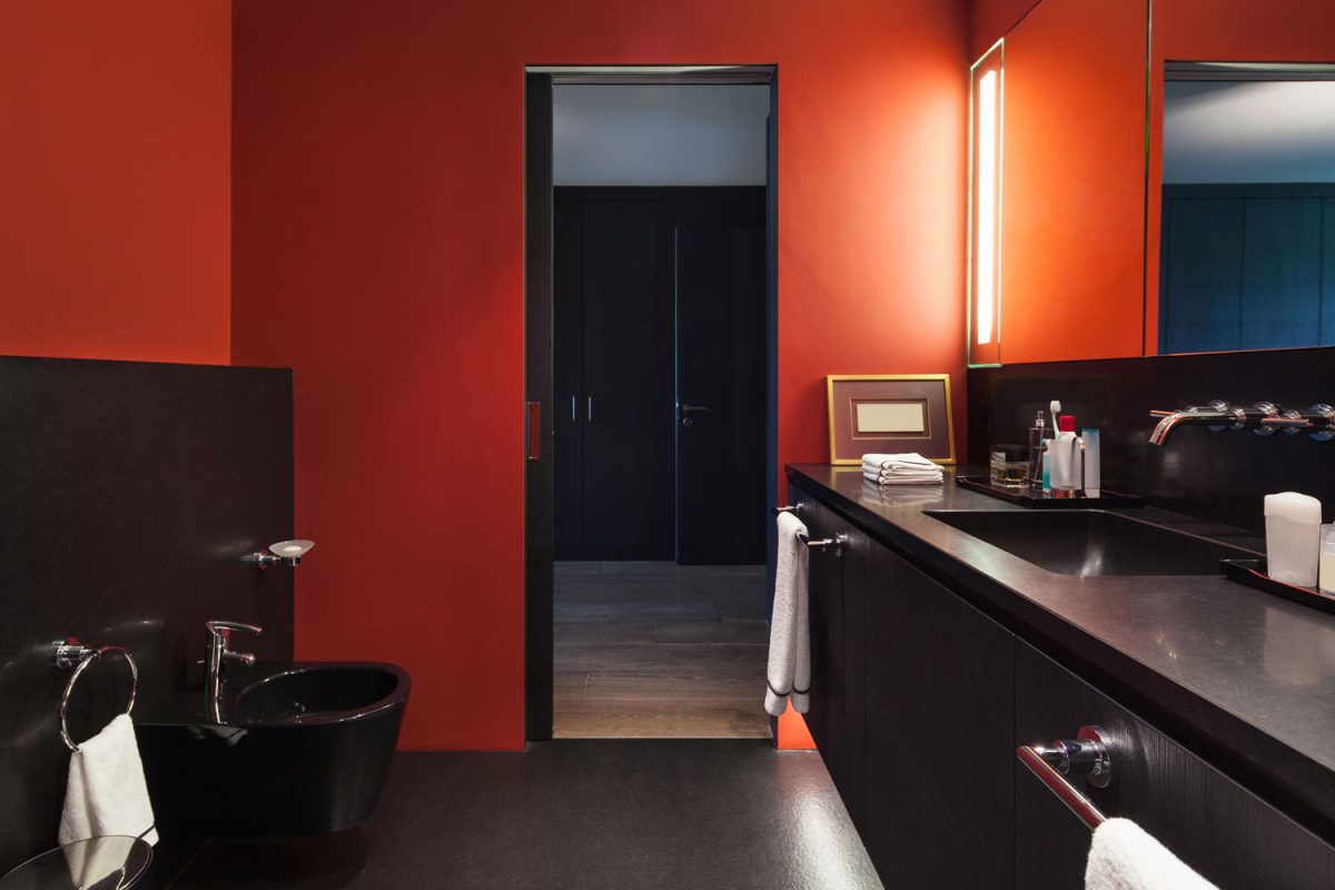 Luxurious black and red combination of a bathroom with a black countertop and a long span mirror