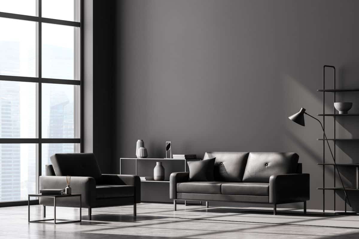 Modern living room interior, black wall and panoramic window with Singapore city view. Dark grey sofa and armchair, coffee table, bookshelves, lamp and chest of drawers