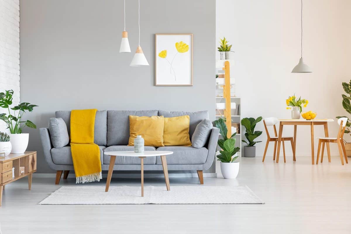 Orange blanket on grey sofa in modern apartment interior with poster and wooden table