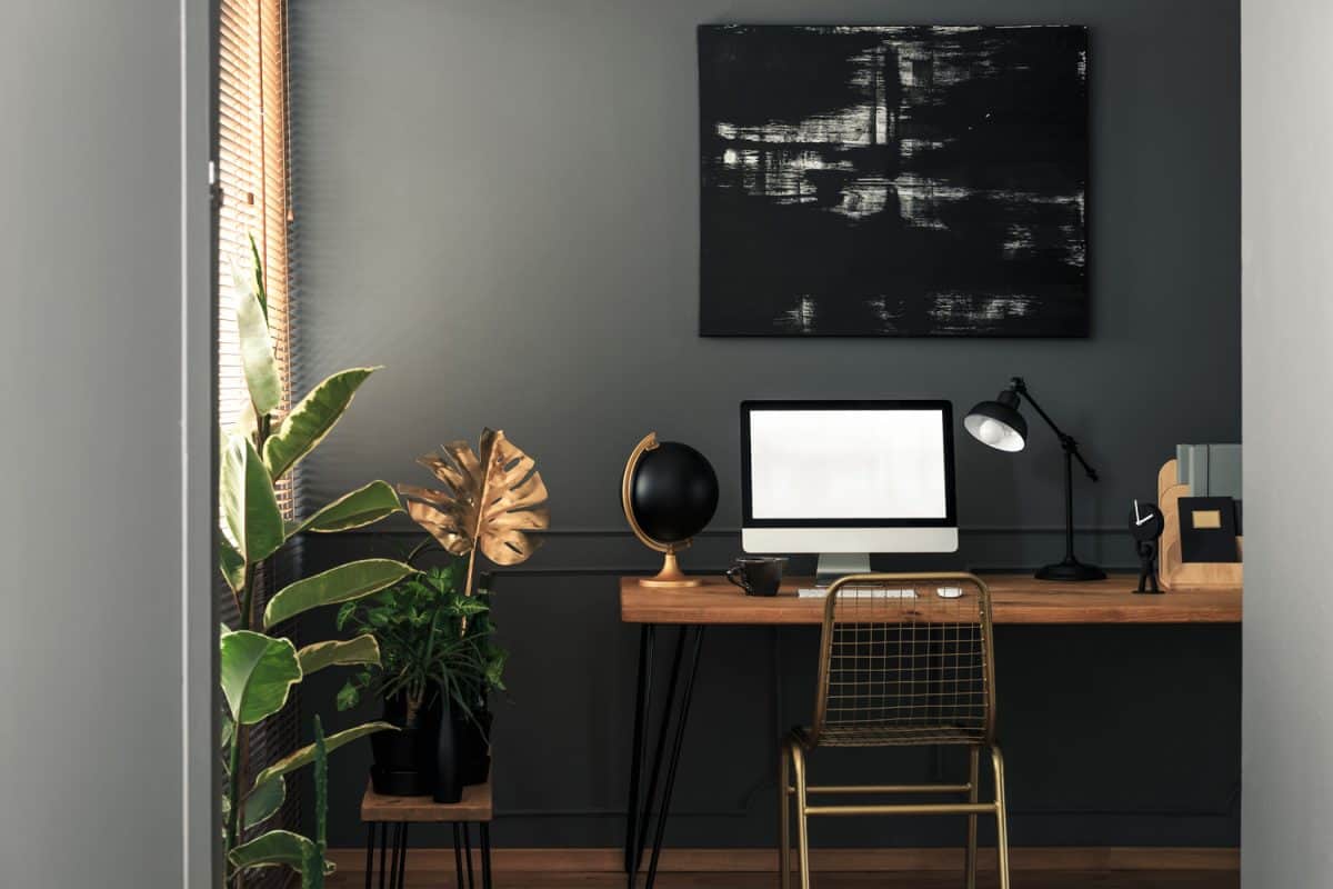Painting above desk with computer desktop and lamp in grey and gold workspace interior