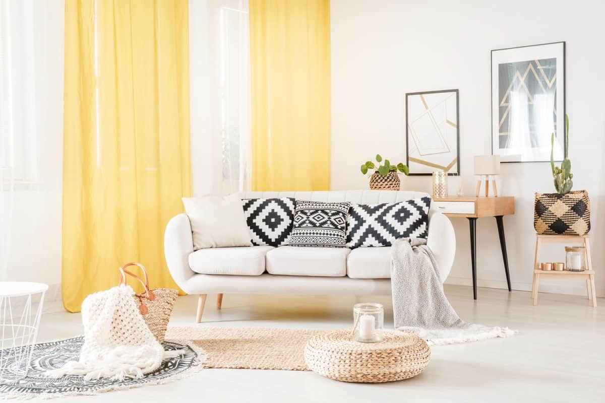 Pillows with geometric pattern lying on a white sofa in cozy living room with yellow curtains