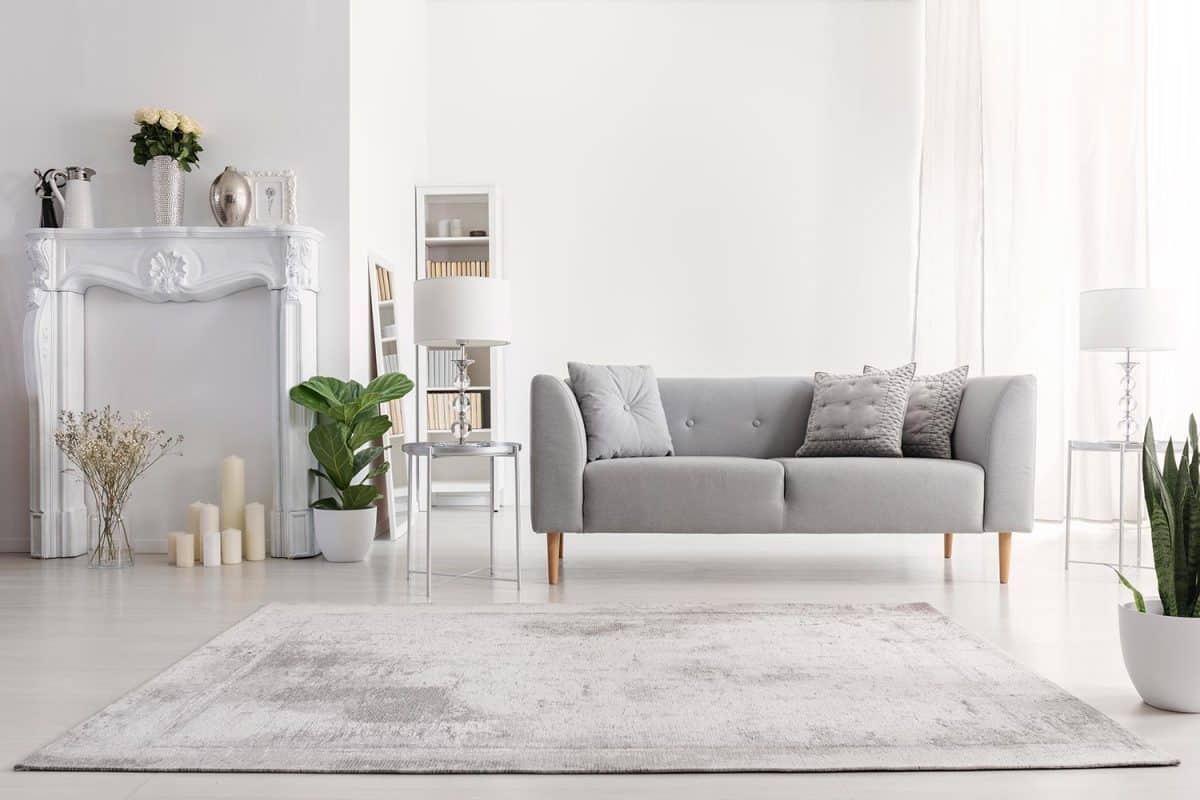 Plants and carpet in white living room interior with candles next to grey couch