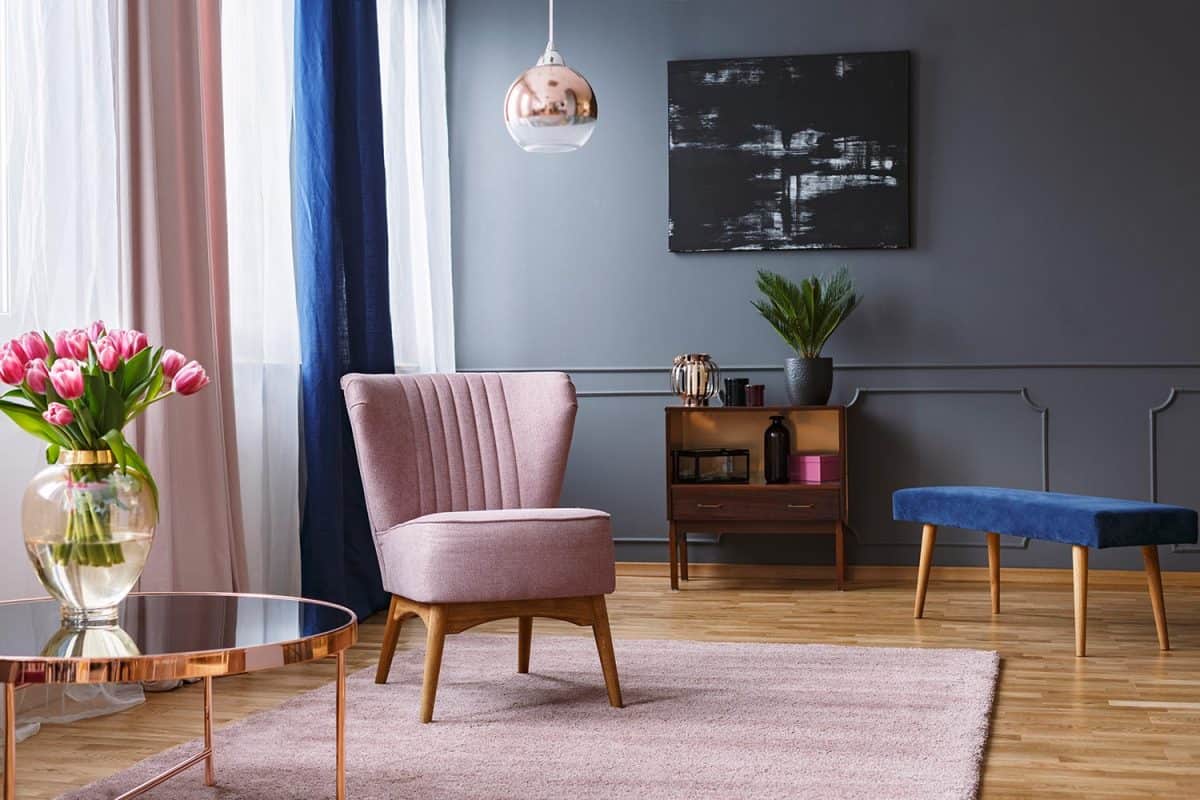 Real photo of a pink armchair standing on a rug and under a lamp in spacious living room