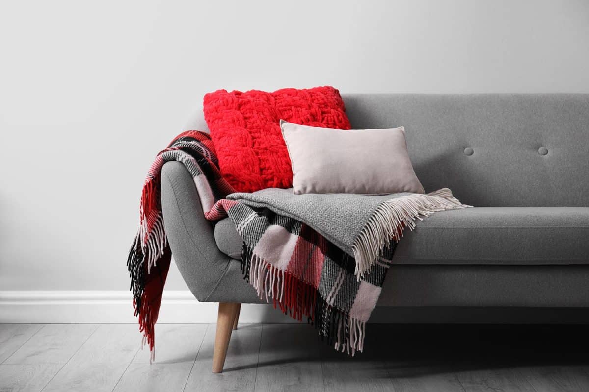 Sofa with soft pillows and warm plaids near light wall