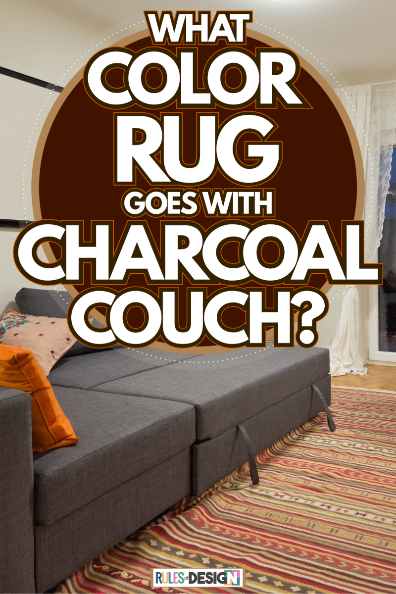 A charcoal colored sectional sofa with orange throw pillows and a multi colored rug on the wooden flooring, What Color Rug Goes With Charcoal Couch?