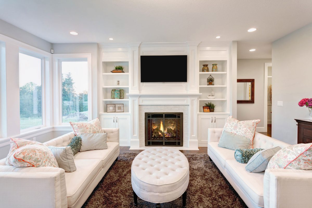 White designed living room with white couches and a fireplace with TV on top of the mantel