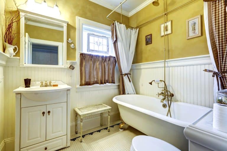Yellow old bathroom interior with white plank paneled wall trim and antique vanity and bath tub, Can You Use Wall Paneling In A Bathroom? [Is It Waterproof?]