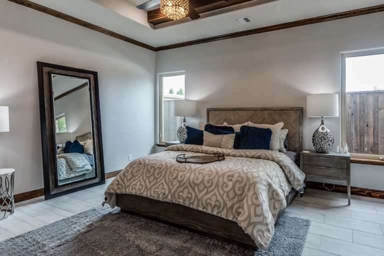 A bedroom evenly spaced out with gorgeous beddings with huge windows on the side and a full length mirror on the side, How High Should You Hang A Full-Length Mirror?
