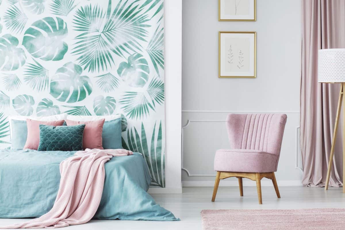 A floral designed header wall and a bed with teal and pink beddings matched with a small pink chair on the side