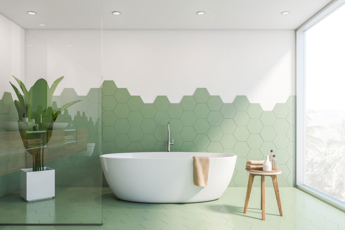 A glass wall shower area with a white bathtub and hexagonal tile backsplash