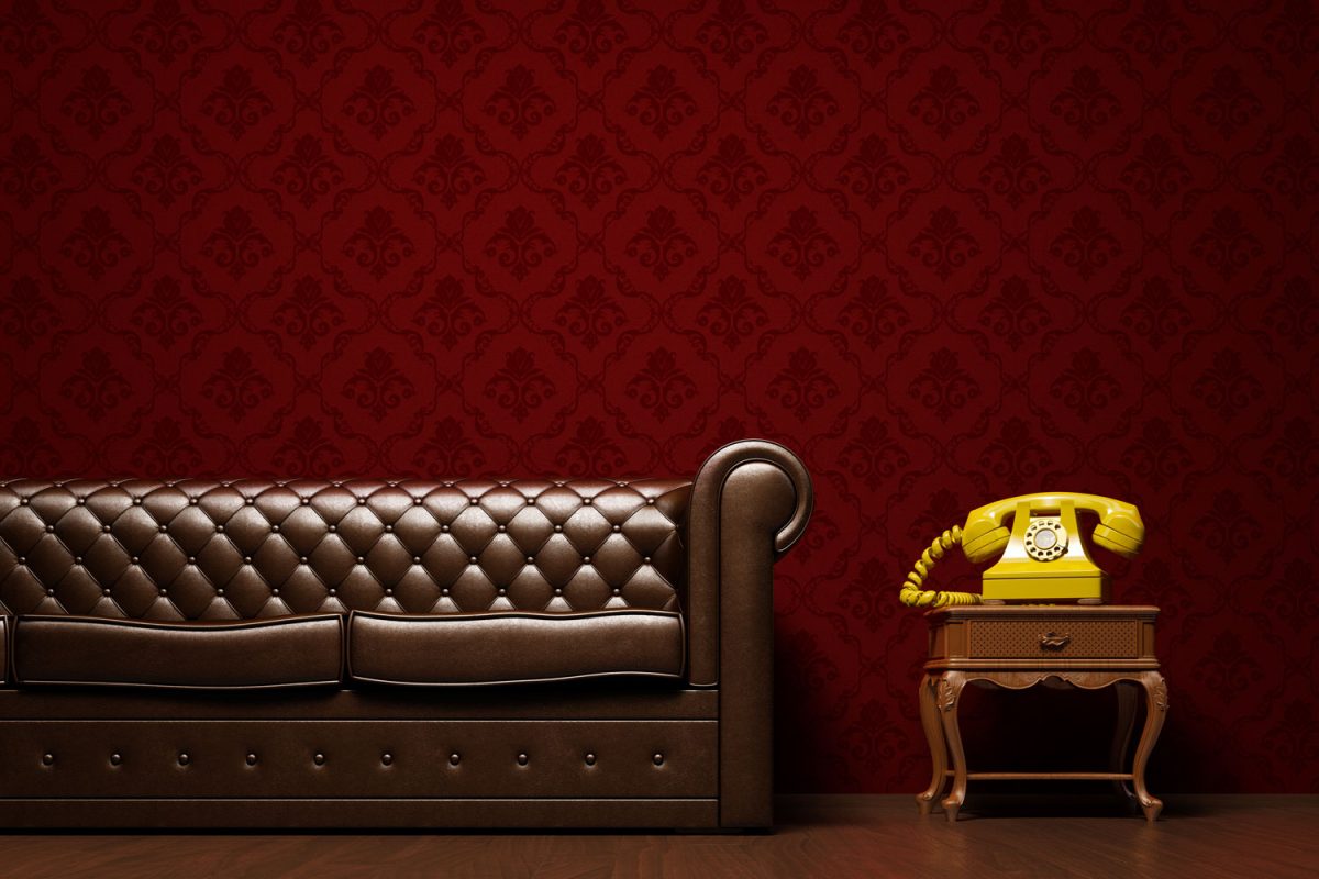 A long brown leather sofa with a small end table matched with a yellow phone